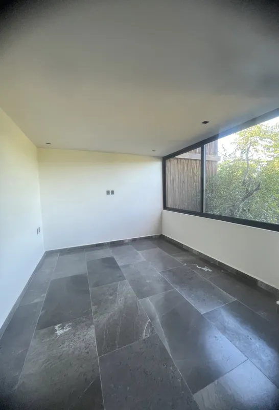 A modern kitchen in a Humana residential unit, featuring dark tiled floors, dark wood and grey cabinets, a stainless steel refrigerator, an integrated oven, and a black countertop with a sink and faucet. A large window is visible on the right.
