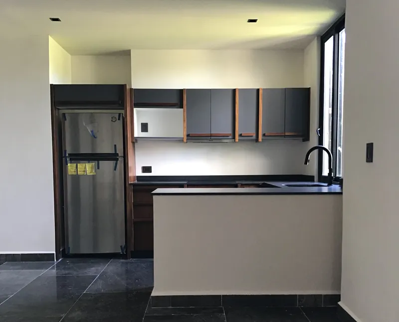 A series of interior photographs from Humana's finished model units, featuring dark grey tiled floors, white walls, wooden built-in furniture, a modern kitchen with stainless steel appliances, and balconies offering views of lush tropical vegetation.