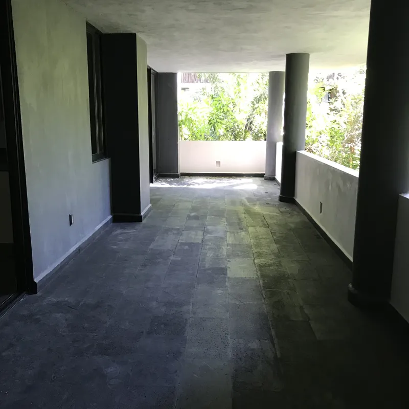A modern kitchen in a Humana model unit, featuring dark grey floor tiles, white walls, grey upper and dark wood lower kitchen cabinets, a stainless steel refrigerator, a black countertop island, and a large window providing natural light.