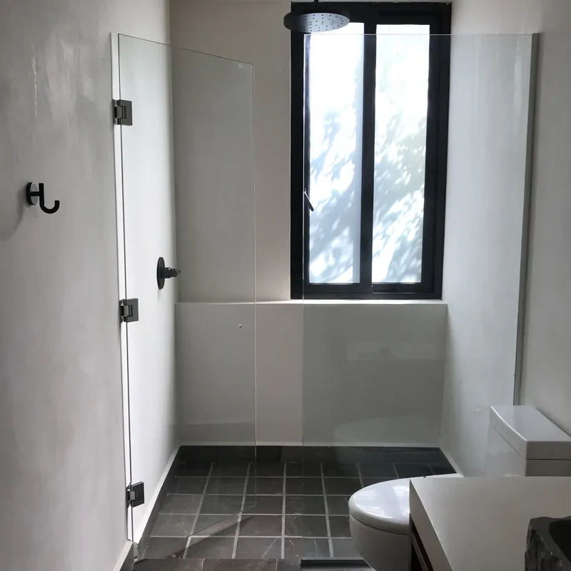 A modern kitchen in a Humana model unit, featuring dark grey floor tiles, white walls, grey upper and dark wood lower kitchen cabinets, a stainless steel refrigerator, a black countertop island, and a large window providing natural light.