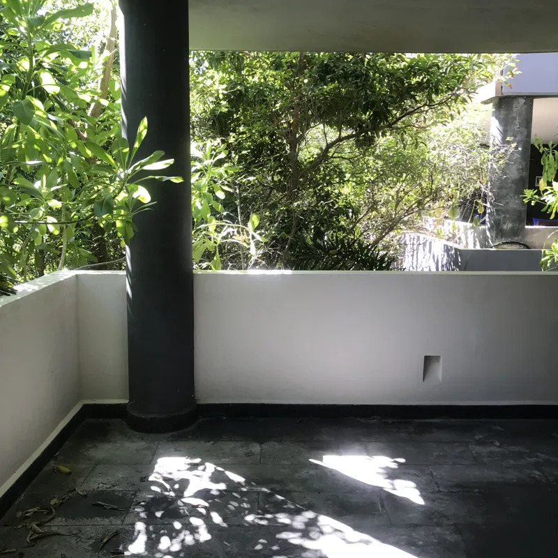 A modern kitchen in a Humana model unit, featuring dark grey floor tiles, white walls, grey upper and dark wood lower kitchen cabinets, a stainless steel refrigerator, a black countertop island, and a large window providing natural light.