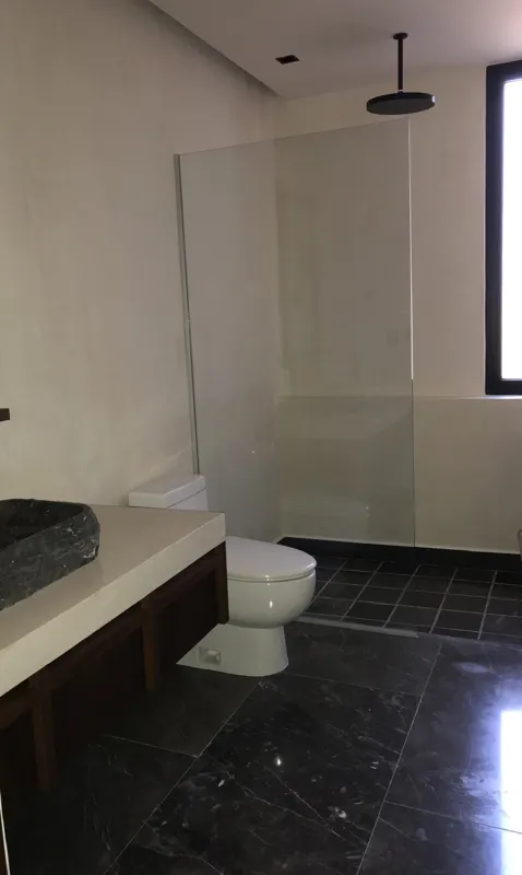 A modern kitchen in a Humana model unit featuring dark cabinetry, black countertops, a stainless steel refrigerator, and dark tiled floors, with large windows offering views of lush greenery.