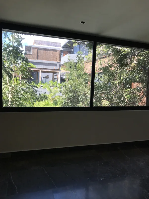 A modern kitchen in a Humana model unit featuring dark cabinetry, black countertops, a stainless steel refrigerator, and dark tiled floors, with large windows offering views of lush greenery.