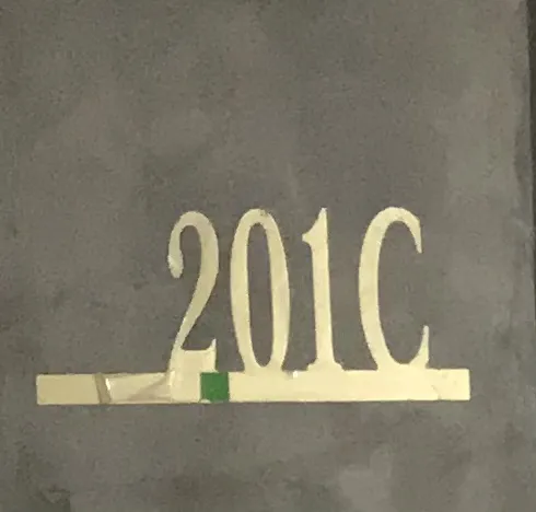 A modern kitchen in a Humana model unit featuring dark cabinetry, black countertops, a stainless steel refrigerator, and dark tiled floors, with large windows offering views of lush greenery.