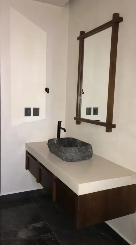 A modern kitchen in a Humana model unit featuring dark cabinetry, black countertops, a stainless steel refrigerator, and dark tiled floors, with large windows offering views of lush greenery.