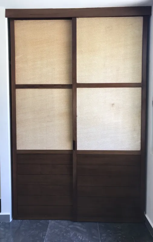 A modern kitchen in a Humana model unit featuring dark cabinetry, black countertops, a stainless steel refrigerator, and dark tiled floors, with large windows offering views of lush greenery.