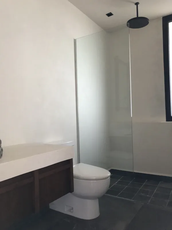 Interior view of a finished residential unit at Humana Tulum, featuring dark polished marble floors, white walls, a built-in wooden closet with sliding doors, an air conditioning unit, and a modern bathroom with a unique stone basin, black fixture...