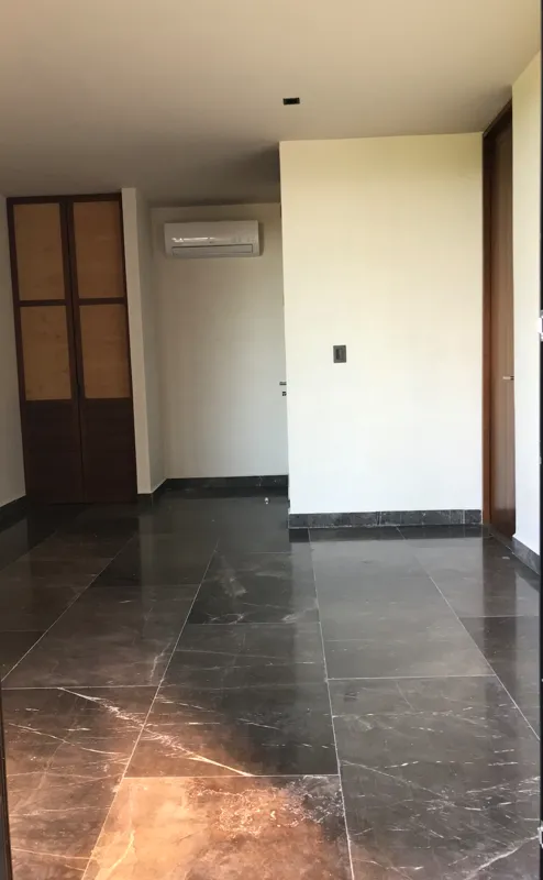 Interior view of a finished residential unit at Humana Tulum, featuring dark polished marble floors, white walls, a built-in wooden closet with sliding doors, an air conditioning unit, and a modern bathroom with a unique stone basin, black fixture...