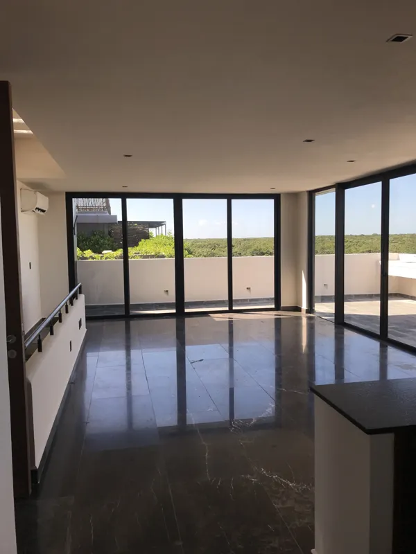 Interior view of a finished residential unit at Humana Tulum, featuring dark polished marble floors, white walls, a built-in wooden closet with sliding doors, an air conditioning unit, and a modern bathroom with a unique stone basin, black fixture...