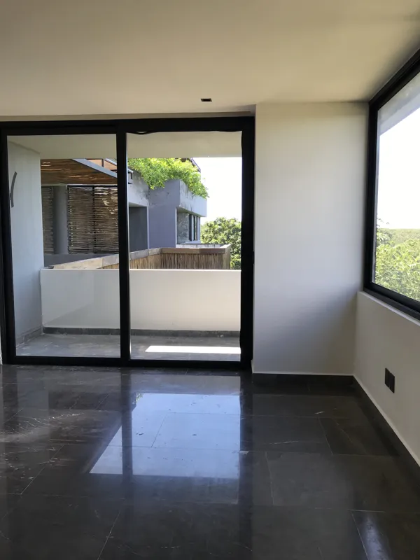 Interior view of a finished residential unit at Humana Tulum, featuring dark polished marble floors, white walls, a built-in wooden closet with sliding doors, an air conditioning unit, and a modern bathroom with a unique stone basin, black fixture...