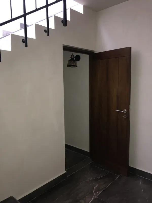 Interior view of a finished residential unit at Humana Tulum, featuring dark polished marble floors, white walls, a built-in wooden closet with sliding doors, an air conditioning unit, and a modern bathroom with a unique stone basin, black fixture...