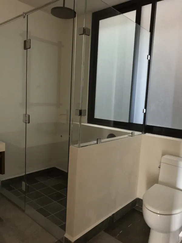 Interior view of a finished residential unit at Humana Tulum, featuring dark polished marble floors, white walls, a built-in wooden closet with sliding doors, an air conditioning unit, and a modern bathroom with a unique stone basin, black fixture...