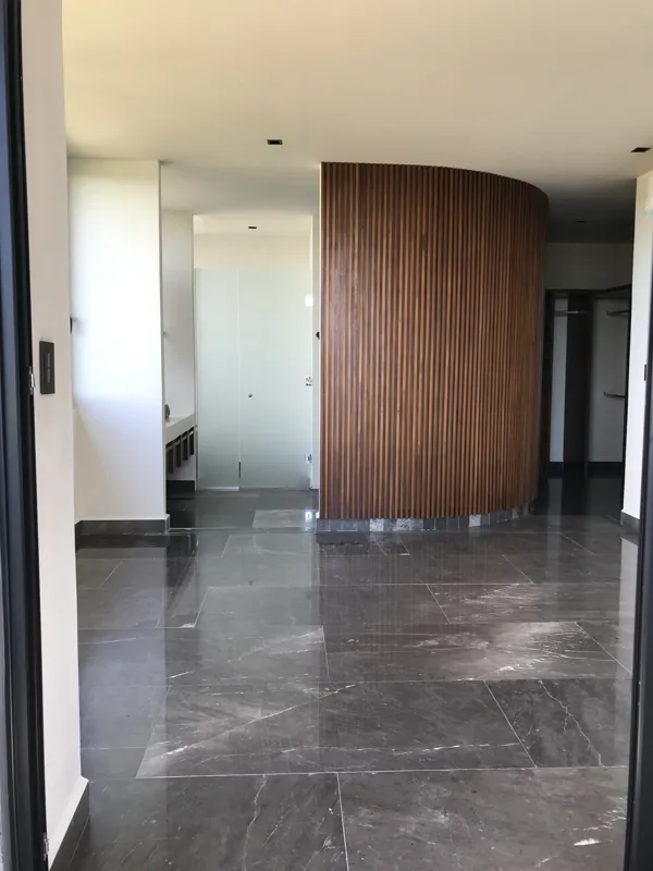 Interior view of a finished residential unit at Humana Tulum, featuring dark polished marble floors, white walls, a built-in wooden closet with sliding doors, an air conditioning unit, and a modern bathroom with a unique stone basin, black fixture...