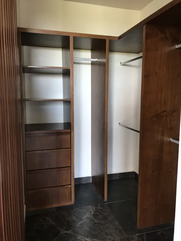Interior view of a finished residential unit at Humana Tulum, featuring dark polished marble floors, white walls, a built-in wooden closet with sliding doors, an air conditioning unit, and a modern bathroom with a unique stone basin, black fixture...