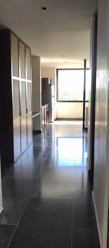 A modern kitchen in Humana's Unit 303D, featuring dark grey upper cabinets, wooden lower cabinets, a black sink, an integrated oven, and a stainless steel refrigerator with protective tape, all set against dark tiled flooring.