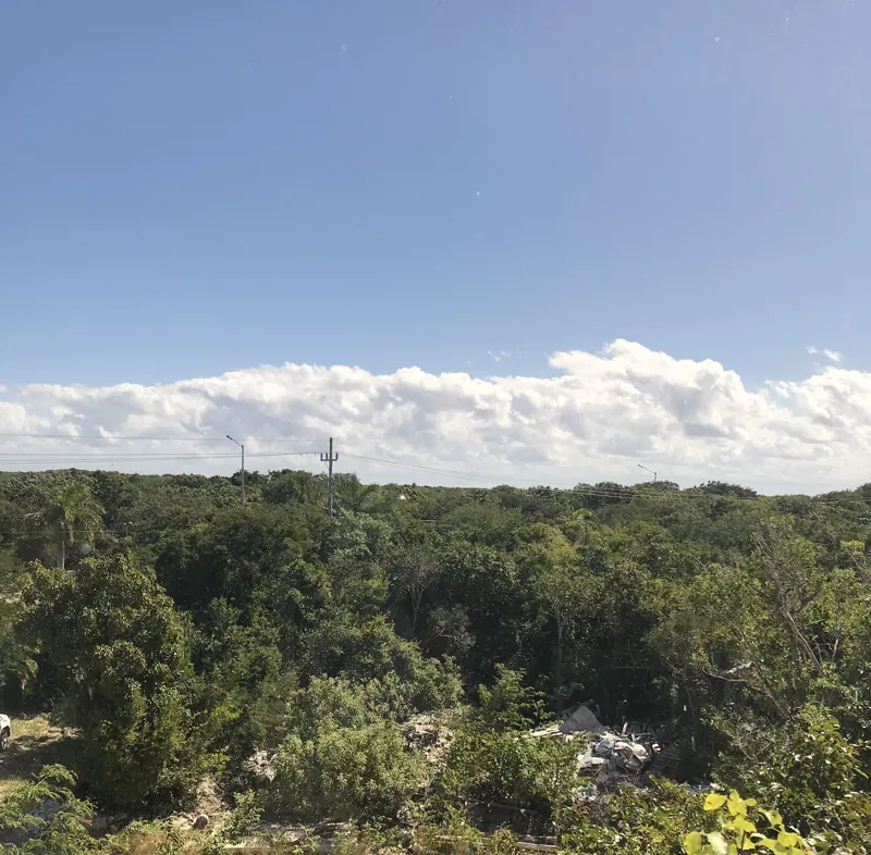 A modern kitchen in Humana's Unit 303D, featuring dark grey upper cabinets, wooden lower cabinets, a black sink, an integrated oven, and a stainless steel refrigerator with protective tape, all set against dark tiled flooring.