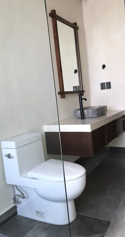 A collection of interior photos from Humana development, featuring a modern bathroom with a unique stone vessel sink, dark wood vanity, and rain shower, alongside a spacious living area with polished grey tiled floors, white walls, and large slidi...