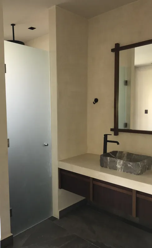 A collection of interior photos from Humana development, featuring a modern bathroom with a unique stone vessel sink, dark wood vanity, and rain shower, alongside a spacious living area with polished grey tiled floors, white walls, and large slidi...