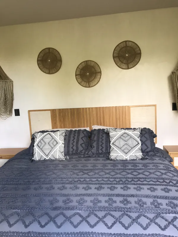 A modern kitchen in a Humana model unit, featuring dark cabinetry, stainless steel appliances, a black sink, a light wood breakfast bar with two woven stools, and decorative wall plates, illuminated by natural light from a window.