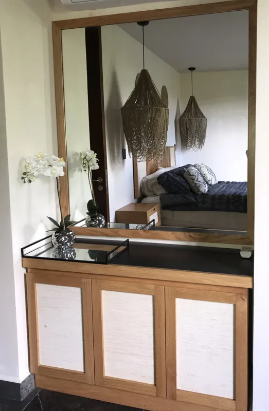 A modern kitchen in a Humana model unit, featuring dark cabinetry, stainless steel appliances, a black sink, a light wood breakfast bar with two woven stools, and decorative wall plates, illuminated by natural light from a window.