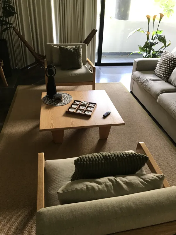 A modern kitchen in a Humana model unit, featuring dark cabinetry, stainless steel appliances, a black sink, a light wood breakfast bar with two woven stools, and decorative wall plates, illuminated by natural light from a window.