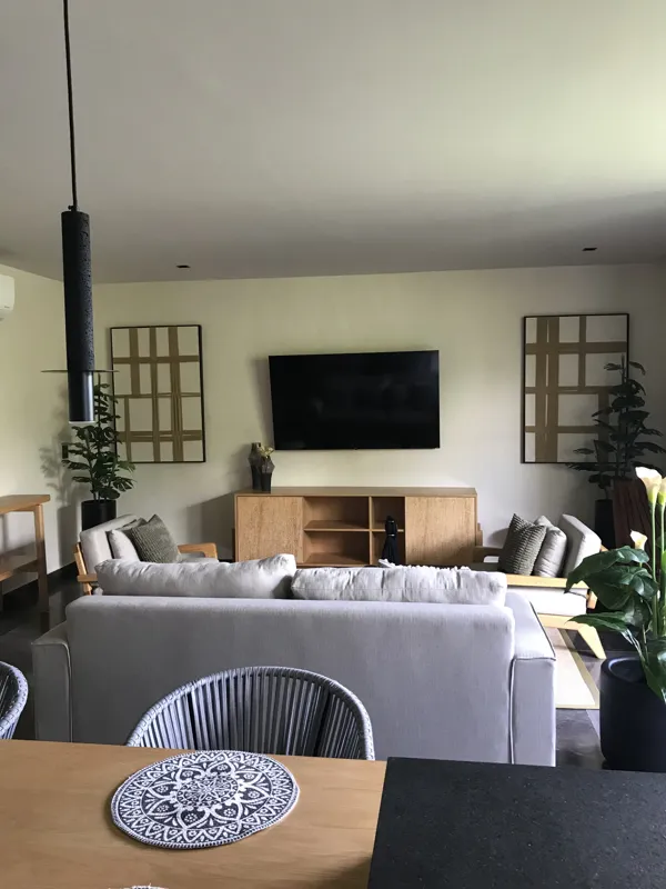 A modern kitchen in a Humana model unit, featuring dark cabinetry, stainless steel appliances, a black sink, a light wood breakfast bar with two woven stools, and decorative wall plates, illuminated by natural light from a window.