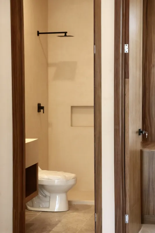 A modern kitchen in an Uxmal unit featuring warm wooden cabinetry, a black countertop with an integrated sink, a built-in oven, microwave, and a round wooden dining table with chairs, all under soft recessed lighting.