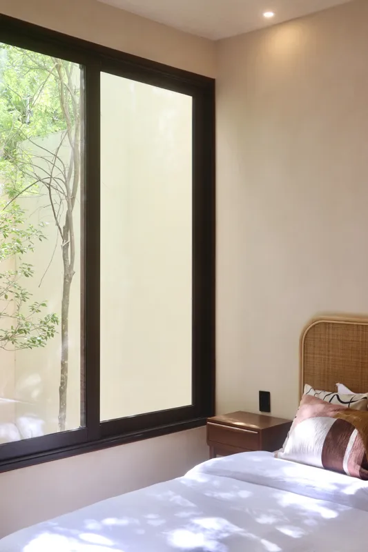 A modern kitchen in an Uxmal unit featuring warm wooden cabinetry, a black countertop with an integrated sink, a built-in oven, microwave, and a round wooden dining table with chairs, all under soft recessed lighting.