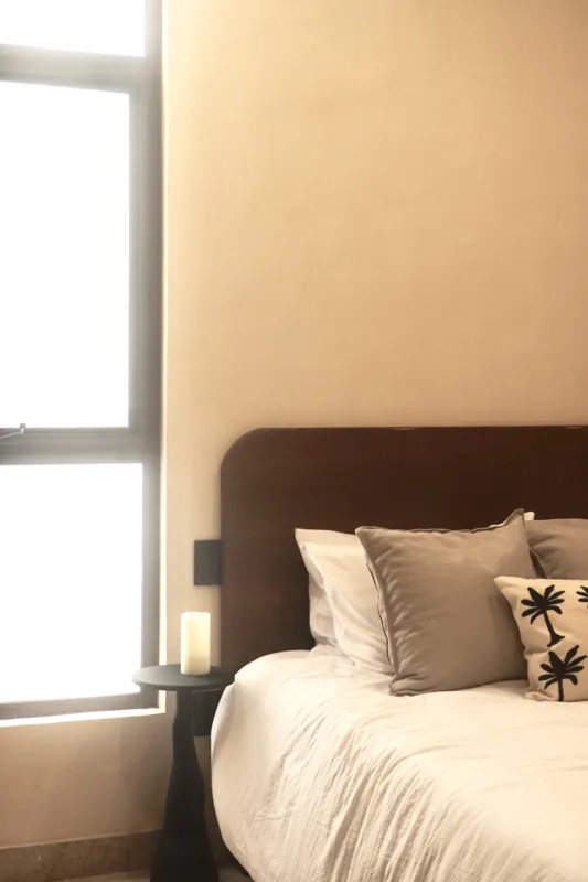A modern kitchen in an Uxmal unit featuring warm wooden cabinetry, a black countertop with an integrated sink, a built-in oven, microwave, and a round wooden dining table with chairs, all under soft recessed lighting.
