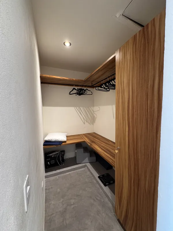 A wide-angle view of a modern apartment's dining area and kitchen in Gold Garden, featuring a round wooden dining table with four chairs, a large woven straw pendant light, and a compact kitchen with concrete countertops and stainless steel applia...