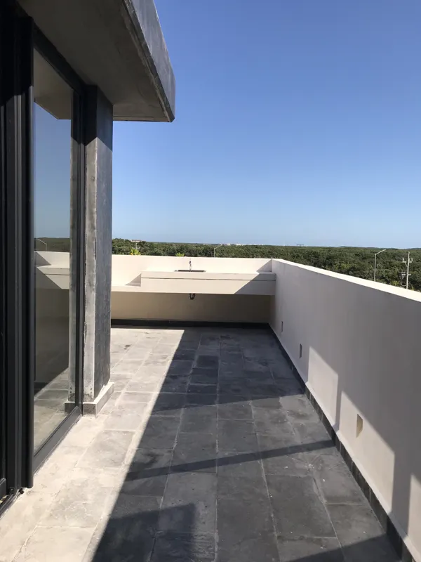 A luxurious rooftop terrace at Humana featuring a built-in jacuzzi with wooden steps, surrounded by modern architecture and lush greenery under a clear blue sky, showcasing finished outdoor amenities.