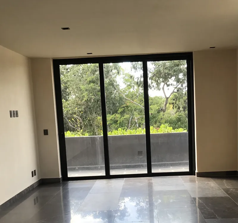A wide interior shot of a finished residential unit at Humana, featuring dark grey marble-patterned floor tiles, a modern kitchen with dark cabinetry, a central wooden island, and a refrigerator wrapped in protective plastic, indicating a complete...