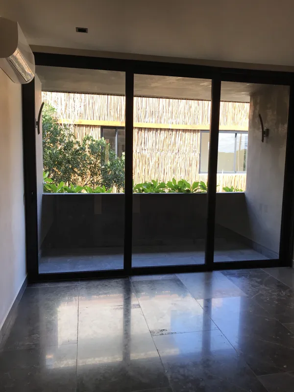 A wide interior shot of a finished residential unit at Humana, featuring dark grey marble-patterned floor tiles, a modern kitchen with dark cabinetry, a central wooden island, and a refrigerator wrapped in protective plastic, indicating a complete...
