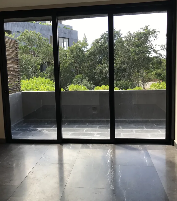 A wide interior shot of a finished residential unit at Humana, featuring dark grey marble-patterned floor tiles, a modern kitchen with dark cabinetry, a central wooden island, and a refrigerator wrapped in protective plastic, indicating a complete...