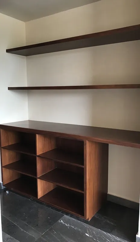 A wide interior shot of a finished residential unit at Humana, featuring dark grey marble-patterned floor tiles, a modern kitchen with dark cabinetry, a central wooden island, and a refrigerator wrapped in protective plastic, indicating a complete...