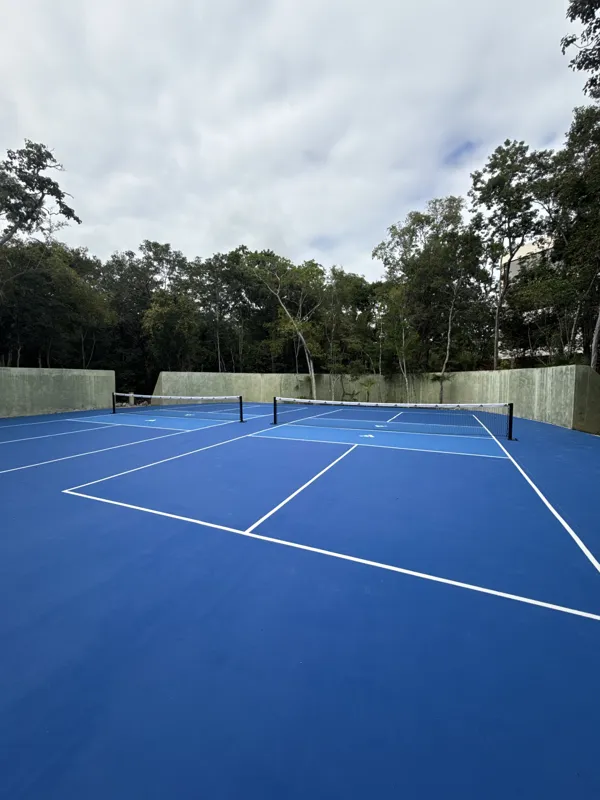 Detailed visual update of Itza Selva's common areas and building exterior. The images show significant construction progress, including the installation of large black-framed glass sliding doors on the main building, ongoing landscaping with grave...