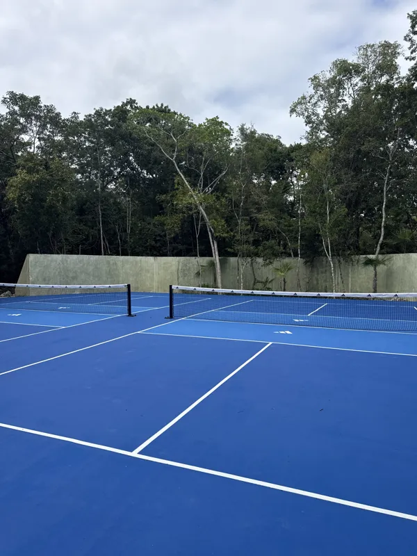 Detailed visual update of Itza Selva's common areas and building exterior. The images show significant construction progress, including the installation of large black-framed glass sliding doors on the main building, ongoing landscaping with grave...