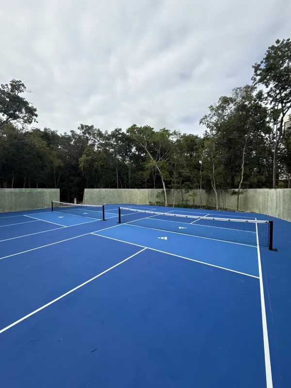 Detailed visual update of Itza Selva's common areas and building exterior. The images show significant construction progress, including the installation of large black-framed glass sliding doors on the main building, ongoing landscaping with grave...