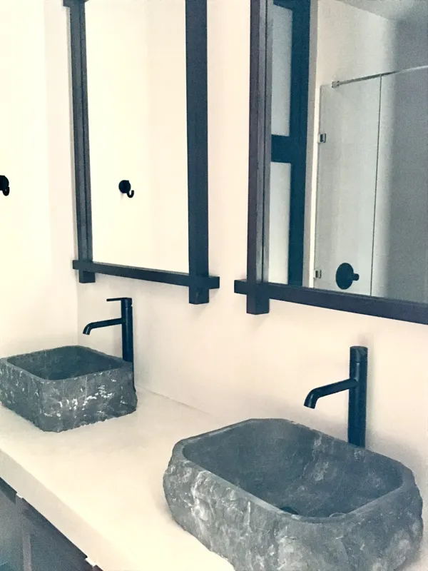 A modern kitchen in a Humana unit, featuring dark cabinetry, a central island with a light countertop, a stainless steel refrigerator still wrapped in protective plastic, and an integrated oven, all set against light-colored walls and dark floor t...