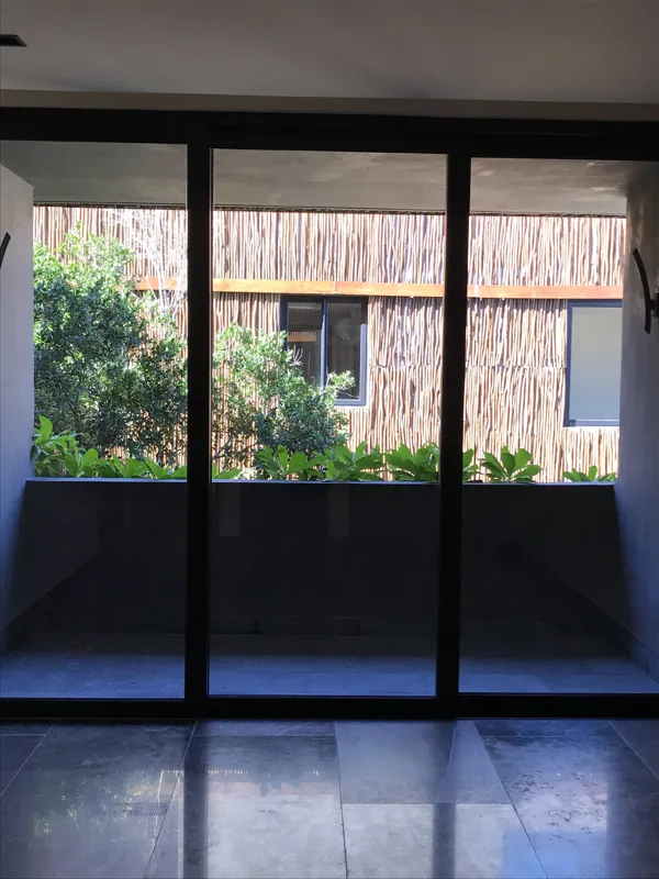 A modern kitchen in a Humana unit, featuring dark cabinetry, a central island with a light countertop, a stainless steel refrigerator still wrapped in protective plastic, and an integrated oven, all set against light-colored walls and dark floor t...