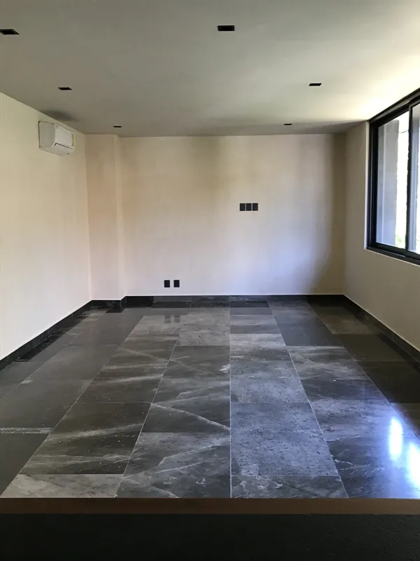 A modern kitchen in a Humana unit, featuring dark cabinetry, a central island with a light countertop, a stainless steel refrigerator still wrapped in protective plastic, and an integrated oven, all set against light-colored walls and dark floor t...