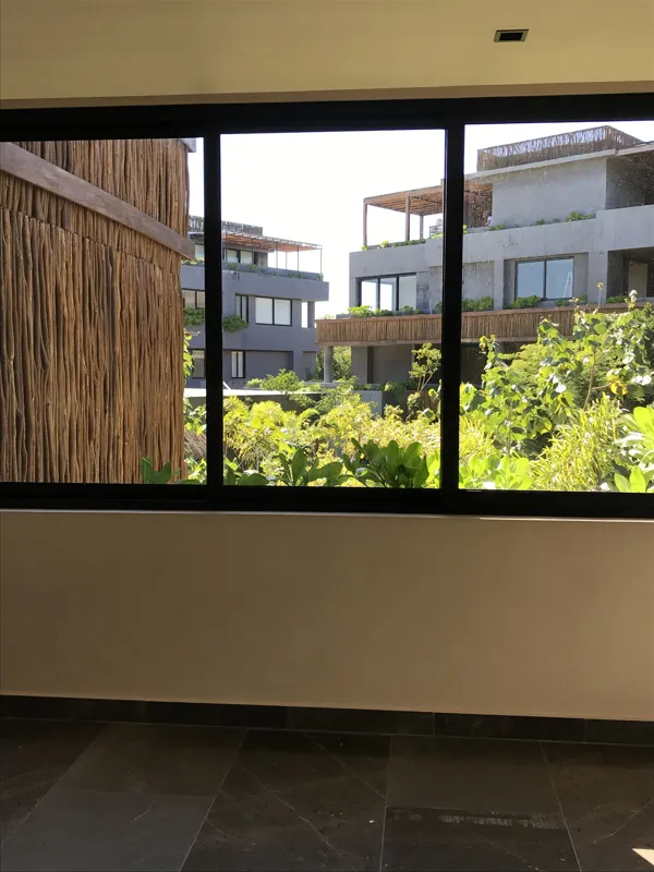 A modern kitchen in a Humana unit, featuring dark cabinetry, a central island with a light countertop, a stainless steel refrigerator still wrapped in protective plastic, and an integrated oven, all set against light-colored walls and dark floor t...