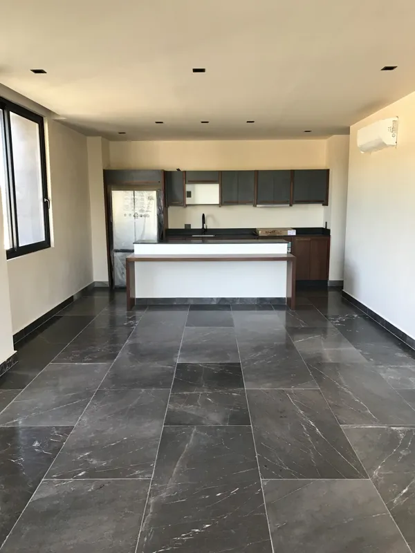 A modern bathroom vanity featuring a dark stone vessel sink, a black faucet, and a rectangular mirror with a dark wooden frame, set above a light-colored countertop and dark wood cabinetry.