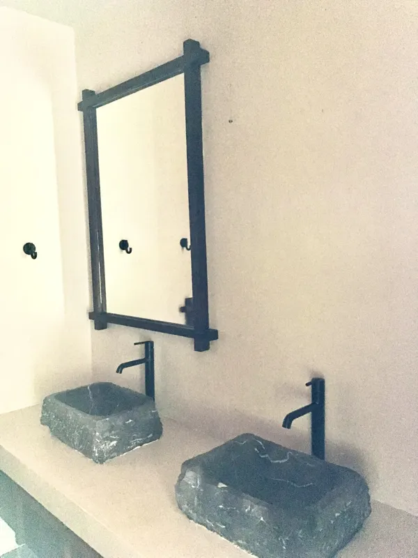 A modern bathroom vanity featuring a dark stone vessel sink, a black faucet, and a rectangular mirror with a dark wooden frame, set above a light-colored countertop and dark wood cabinetry.