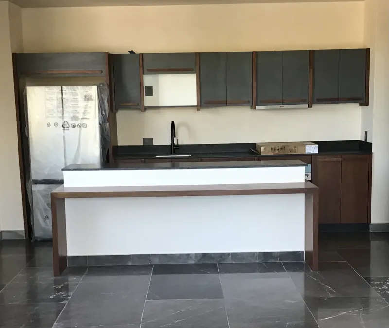 A modern bathroom vanity featuring a dark stone vessel sink, a black faucet, and a rectangular mirror with a dark wooden frame, set above a light-colored countertop and dark wood cabinetry.