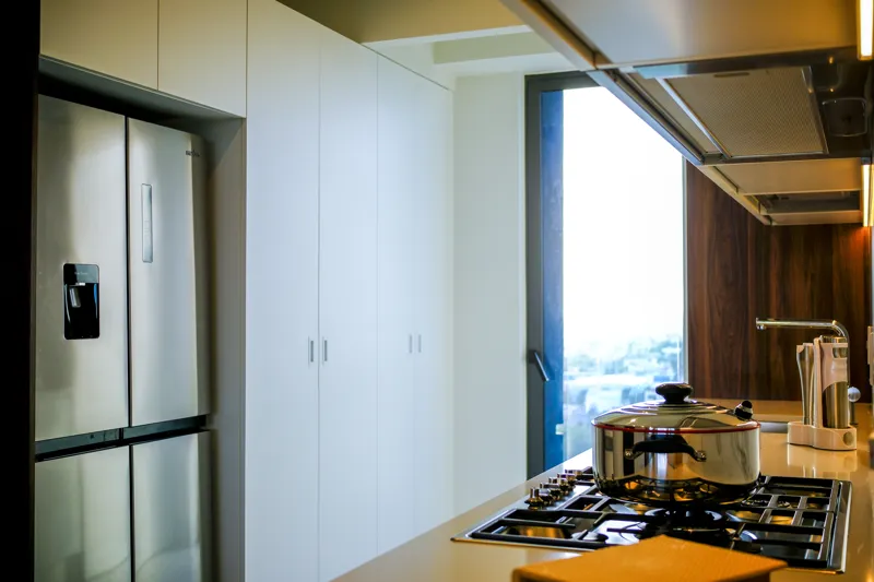 A beautifully furnished living room and balcony in a Woha residence, featuring modern decor, comfortable seating, and a coffee table with pastries, overlooking the Puerto Cancún skyline, a lush golf course, and distant natural reserve.