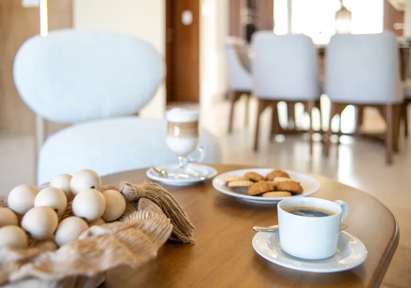 A beautifully furnished living room and balcony in a Woha residence, featuring modern decor, comfortable seating, and a coffee table with pastries, overlooking the Puerto Cancún skyline, a lush golf course, and distant natural reserve.