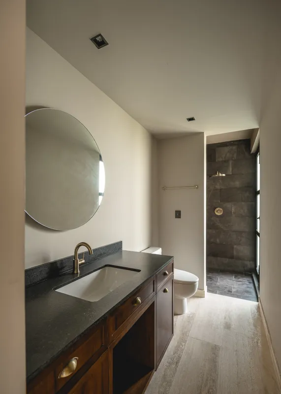 A bright, empty living room in an Arthouse Signature apartment, featuring light-colored tiled floors, an installed air conditioning unit, and expansive sliding glass doors leading to a private balcony with views of a lush tropical landscape and a ...