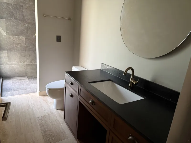 A bright, empty living room in an Arthouse Signature apartment, featuring light-colored tiled floors, an installed air conditioning unit, and expansive sliding glass doors leading to a private balcony with views of a lush tropical landscape and a ...