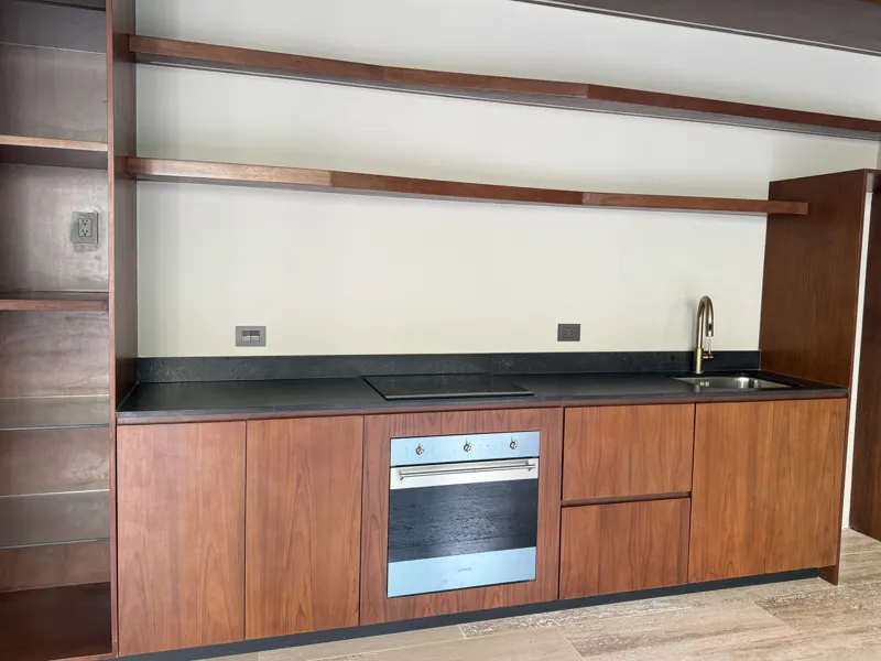 A bright, empty living room in an Arthouse Signature apartment, featuring light-colored tiled floors, an installed air conditioning unit, and expansive sliding glass doors leading to a private balcony with views of a lush tropical landscape and a ...